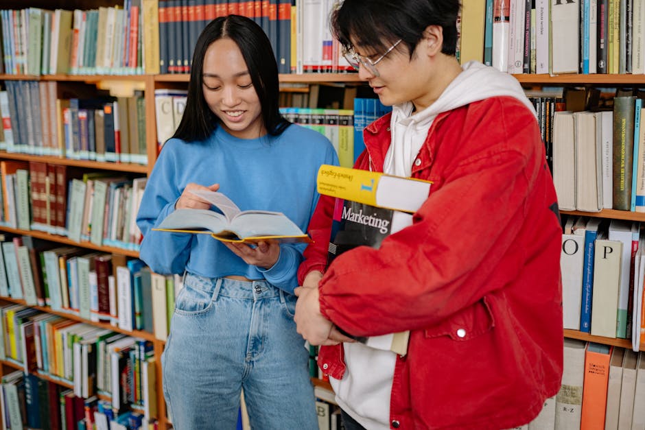 Two students engaged in collaborative study at a university library, sharing books and ideas