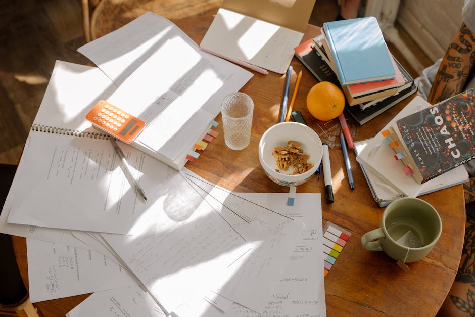 A cluttered study table with books, notes, and study materials in natural light